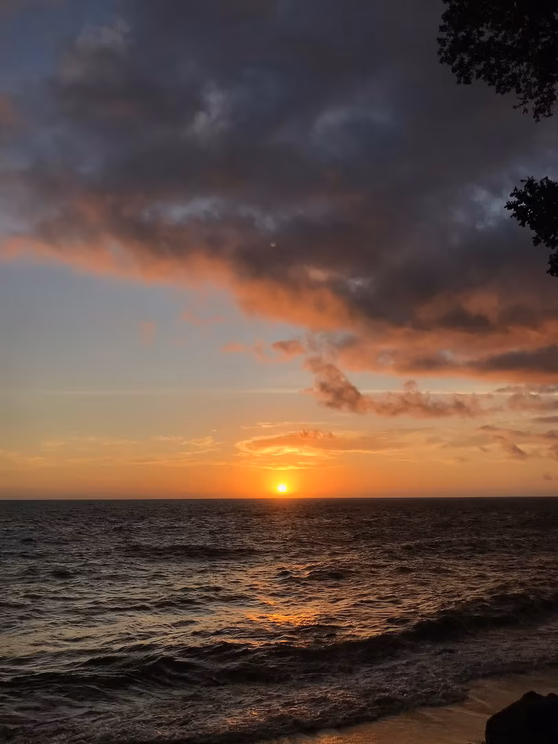 A dramatic ocean sunset with vibrant pink and orange clouds reflected on the water, captured from Ternate Island.
