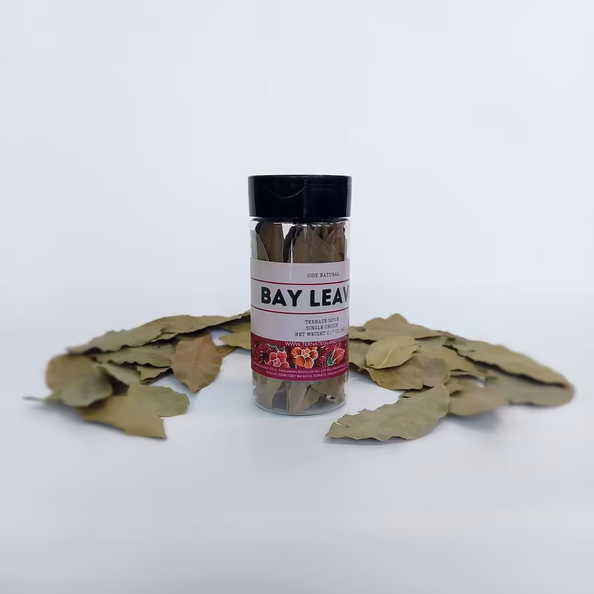 A spice bottle of dried Bay Leaves with a green and red label, accompanied by a scattered handful of whole bay leaves.