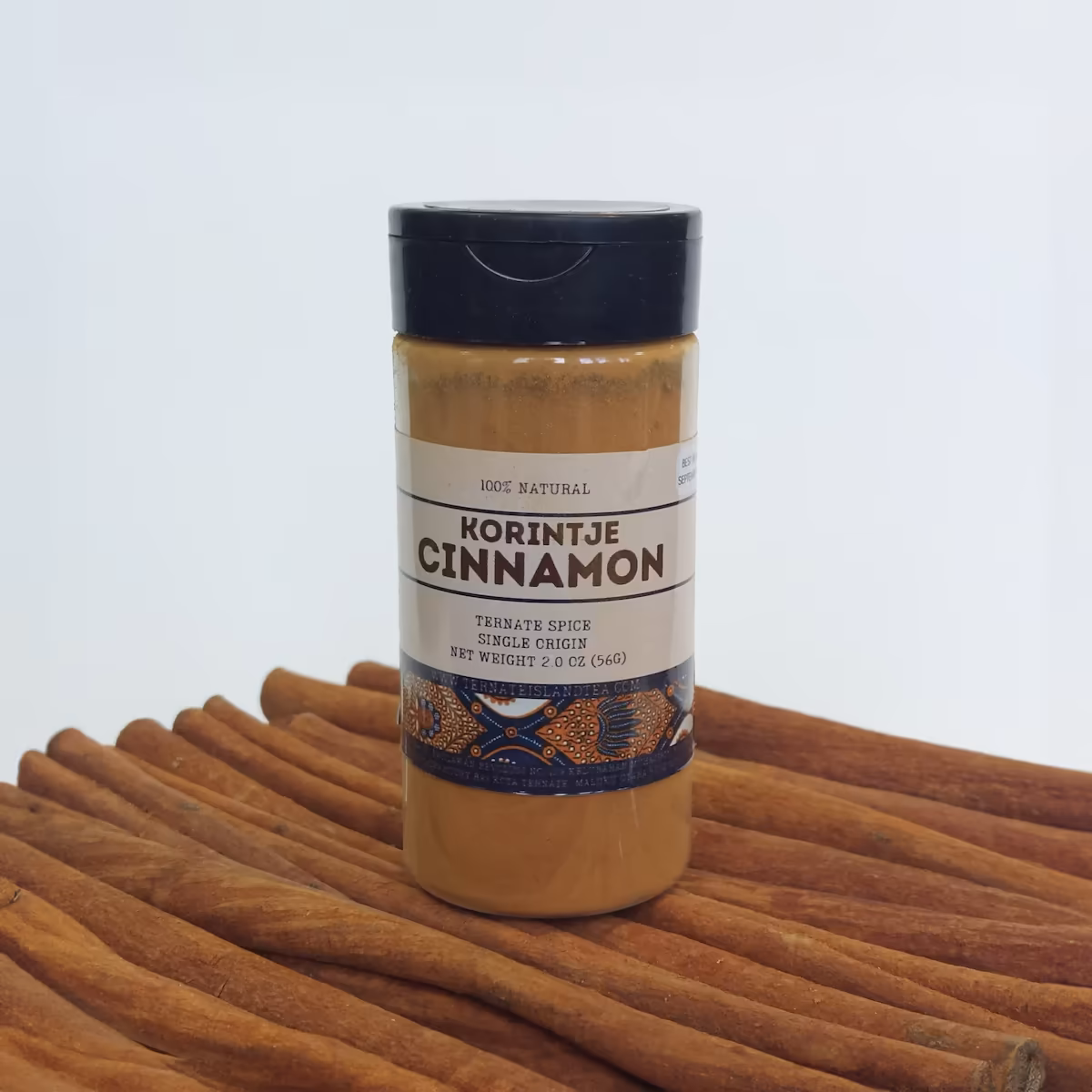 A spice bottle of Korintje Cinnamon powder with a sleek label reading ‘Ternate Spice, Single Origin,’ displayed on rows of whole cinnamon sticks.