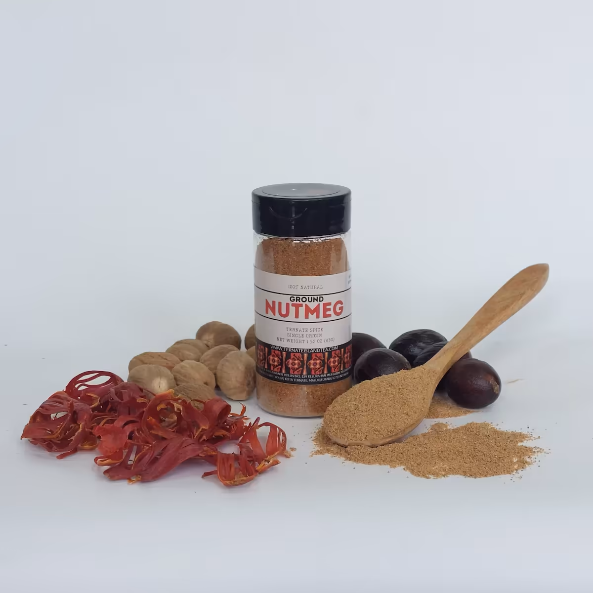 A spice bottle of Ground Nutmeg with a red and white label, displayed alongside whole nutmeg seeds, red mace, and a wooden spoon filled with the powdered spice.