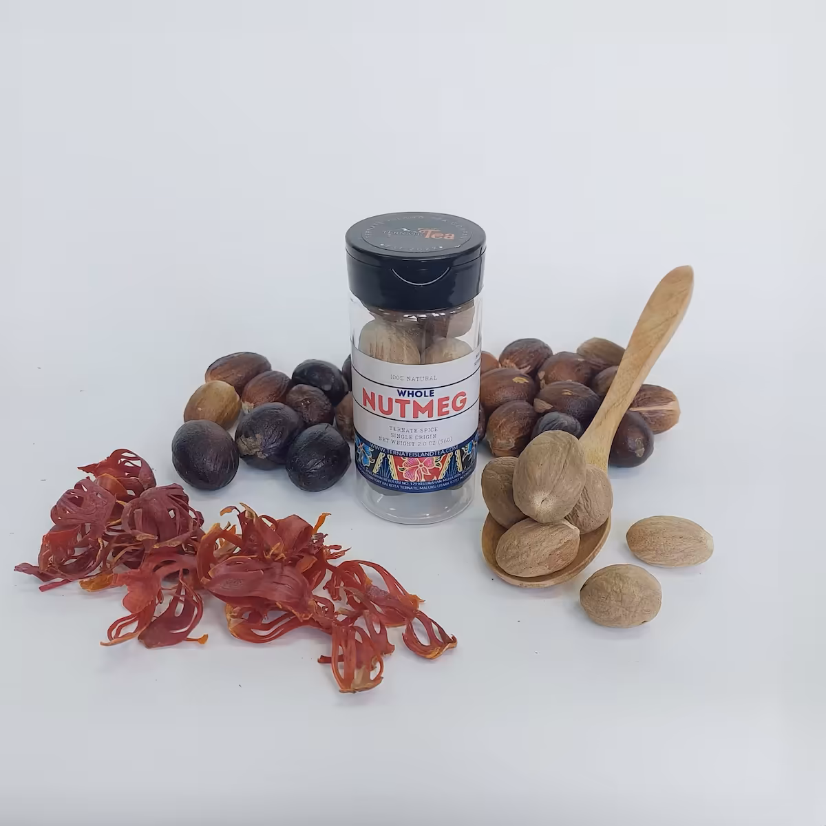 A spice bottle of Whole Nutmeg with a colorful label, surrounded by whole nutmeg seeds, red mace, and a wooden spoon holding whole nutmeg for fresh grating.