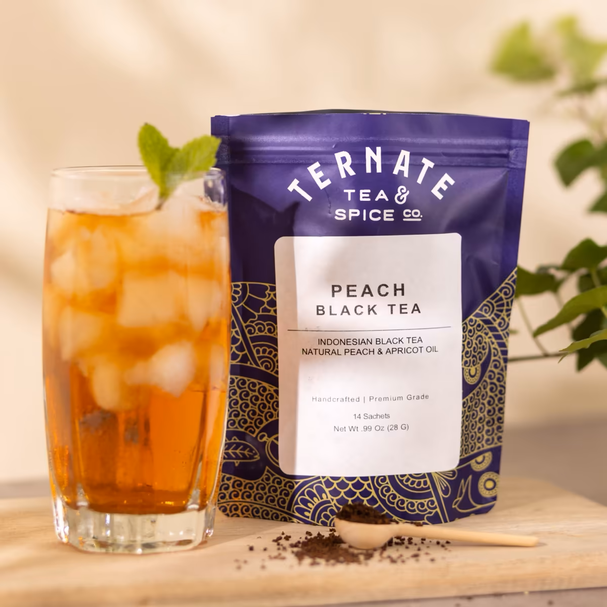 Peach Black Tea in navy and gold packaging, beside a tall glass of the brewed tea over ice garnished with fresh mint.